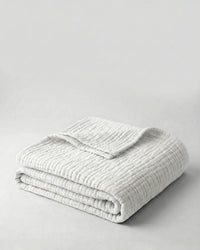 Muslin Blanket in White draped over a bed